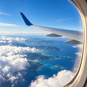 An airplane wing seen through a window above clouds and islands.